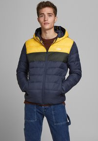Men's zip-up puffer jacket with a yellow, green, and navy color block design. Features a hood, quilted texture, and side pockets.