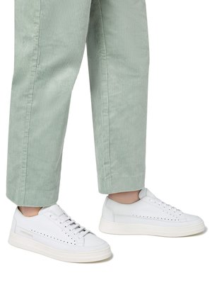 Sneaker bianche in pelle con design perforato, chiusura con lacci e suola spessa in gomma bianca, abbinate a pantaloni di velluto a coste verde menta.