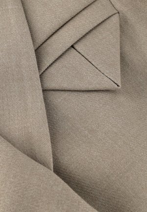 Nahaufnahme von gefaltetem beigem Stoff mit strukturierter Webart, zeigt geschichtete und angewinkelte Falten.