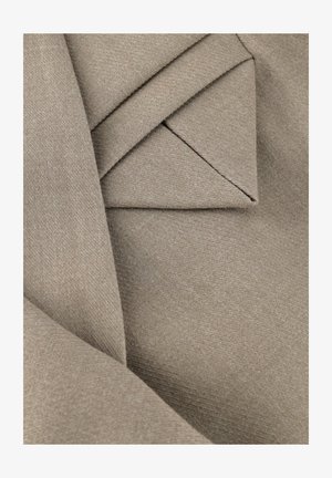 Nahaufnahme von gefaltetem beigem Stoff mit strukturierter Webart, zeigt geschichtete und angewinkelte Falten.