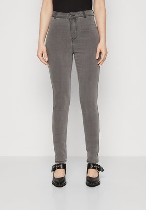 Grå skinny jeans med høy midje, med frontknapplukking og sidelommer, sammen med svarte hæler med spenne.