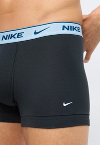 Czarne bokserki z jasnoniebieskim elastycznym pasem. Logo Nike w ciemnym niebieskim na pasie i białym na nodze. Gładka tekstura materiału.