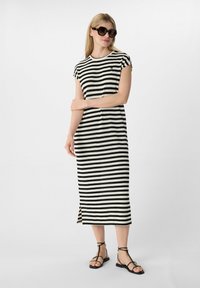 Zwart-wit gestreepte gebreide jurk met cap sleeves, een zijsplit en een rechte pasvorm. Gecombineerd met zwarte sandaaltjes met banden en oversized zonnebril.