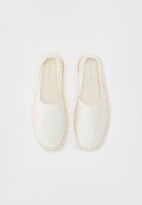 Baltos drobės slip-on bateliai su smėlio spalvos siuvinėjimu aplink padą, pasižymintys lygiu paviršiumi ir minimalistiniu dizainu.