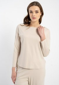 Beżowa bluzka z długim rękawem, wykonana z miękkiego materiału; ma okrągły dekolt, luźny krój oraz boczne rozcięcia, które zapewniają swobodę ruchów i komfort.