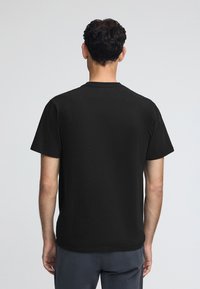 Schwarzes Baumwoll-T-Shirt mit kurzen Ärmeln, klassischem Rundhalsausschnitt und glatter Textur. Keine sichtbaren Logos oder Designs auf der Rückseite.