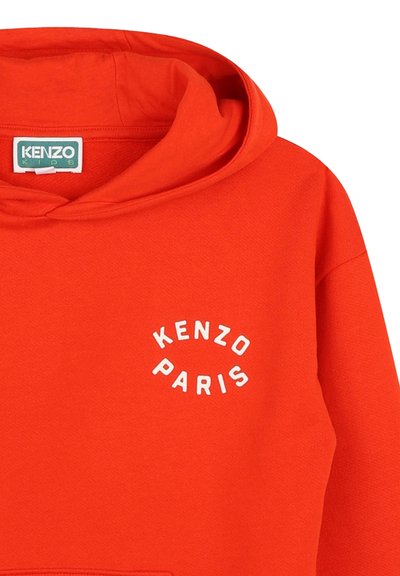 Haut à capuche rouge en tissu doux, arborant un design arrondi blanc "KENZO PARIS" sur la poitrine et une capuche spacieuse.