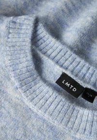 Hellblaues Strickoberteil mit geripptem Rundhalsausschnitt, weicher Textur und einem schwarzen Etikett mit der Aufschrift "LMTD" sowie Größenangaben.