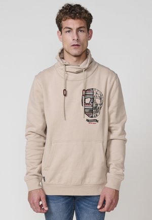Felpa beige con colletto a imbuto e coulisse. Presenta una grafica di teschio colorata e tasca anteriore. Realizzata in un morbido tessuto testurizzato.