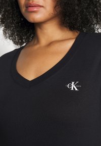 Černé tričko s výstřihem do V z bavlněné směsi, s malým bílým logem Calvin Klein Jeans na levém hrudi. Hladká textura a přiléhavý střih.