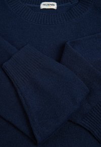 Pull en maille bleu marine avec un col et des poignets côtelés, présentant une texture douce et une étiquette indiquant "TEZENIS KIDS."