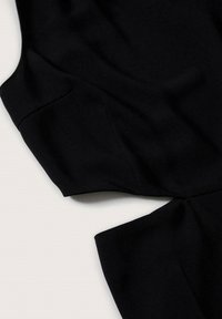 Vêtement en textile noir à la texture lisse, présentant une épaule structurée et un design drapé, soulignés par des détails de coutures angulaires.