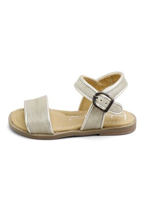 Sandalia infantil de punta abierta con tiras metálicas beige, hebilla en el tobillo, plantilla acolchada y suela plana marrón.