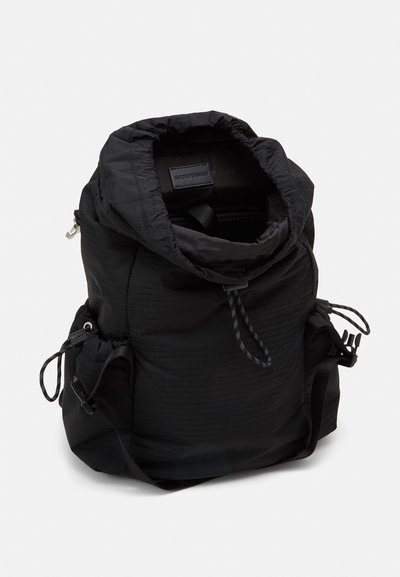 Zaino in nylon nero con parte superiore arricciata, cordini regolabili e tasche esterne laterali. L'interno presenta una texture liscia con un marchio.