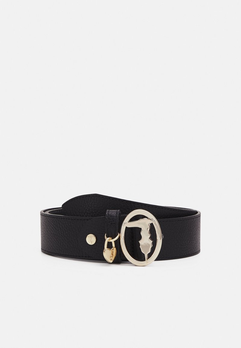 Ceinture en cuir noir texturé avec une boucle ovale dorée présentant une figure stylisée et un petit charm en forme de cœur doré.