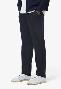 Marineblauwe broek met een ontspannen pasvorm en zijzakken, gemaakt van gladde stof. Gepaard met witte sneakers met lichte accenten.