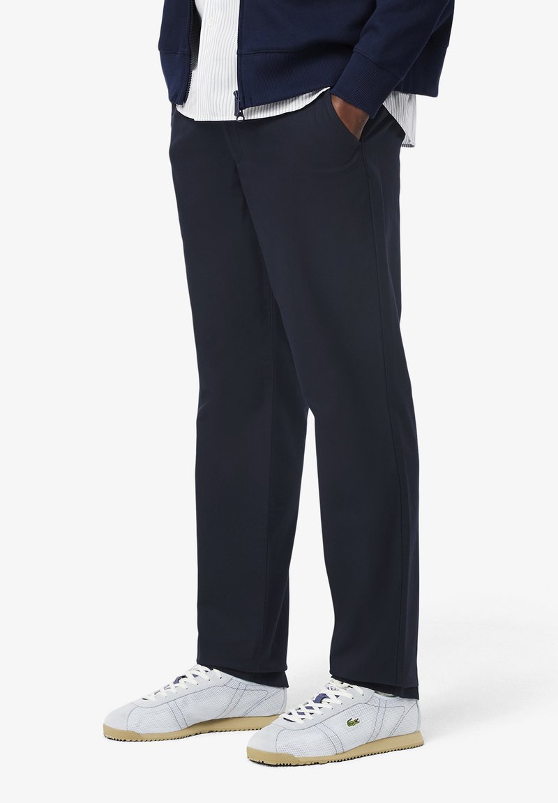 Marineblauwe broek met een ontspannen pasvorm en zijzakken, gemaakt van gladde stof. Gepaard met witte sneakers met lichte accenten.