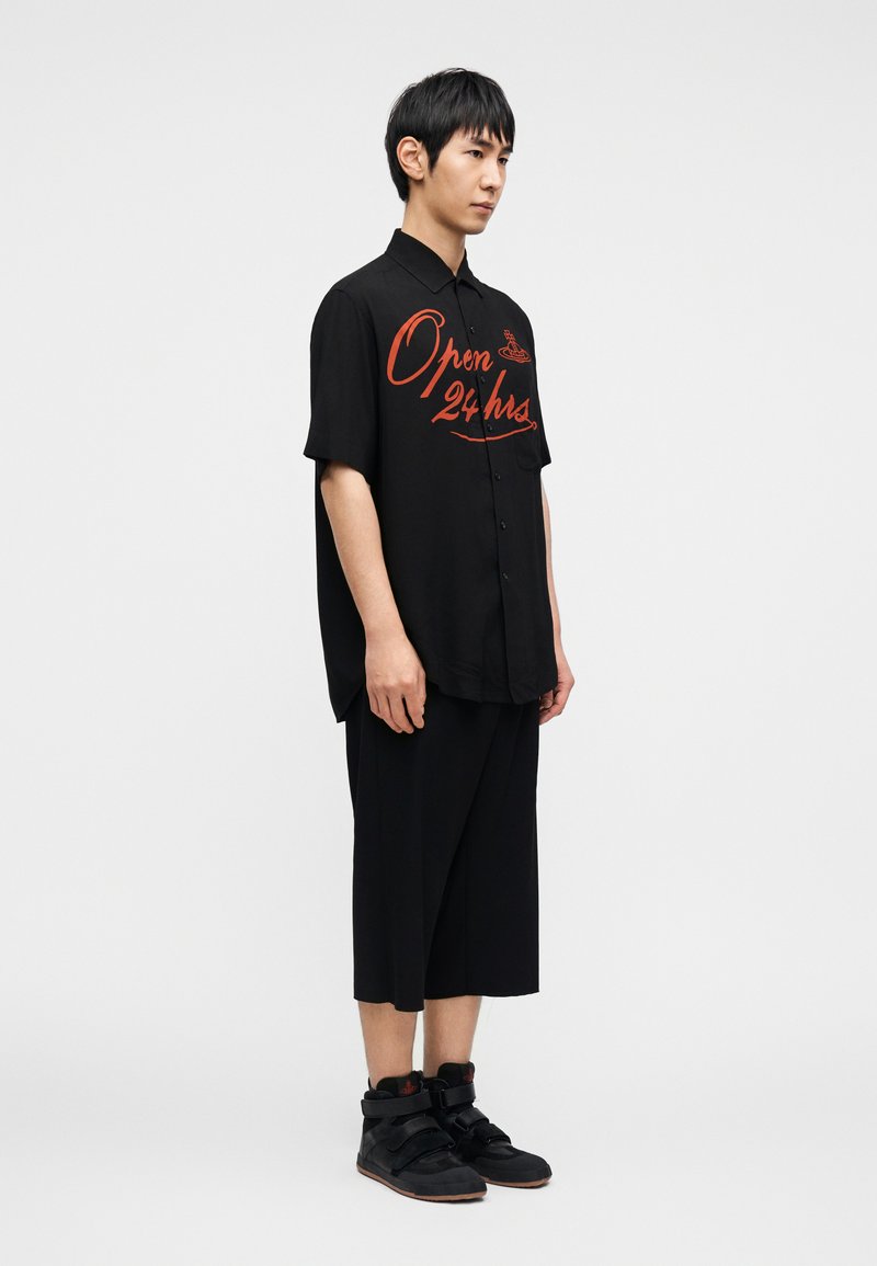 Chemise noire à manches courtes avec un graphisme rouge « Open 24 hrs », associée à un short noir ample et des chaussures de sport montantes noires.