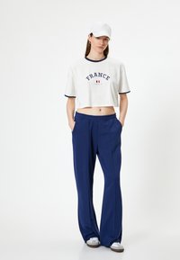 Hvid cropped t-shirt med marineblå kanter og "FRANCE" tryk, parret med løse marineblå bukser og hvide sneakers med elastisk talje.