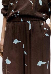 Tenue en tissu marron avec motif floral bleu ; design décontracté avec une taille élastique et des détails plissés ; texture légère.