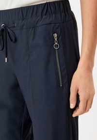 Navy blauwe broek gemaakt van lichtgewicht stof met een elastische tailleband en trekkoord; heeft een ritszak en een soepele textuur.