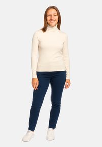 Top a collo polo color crema abbinato a pantaloni slim-fit blu navy e sneaker bianche. Texture liscia, design aderente e maniche lunghe.