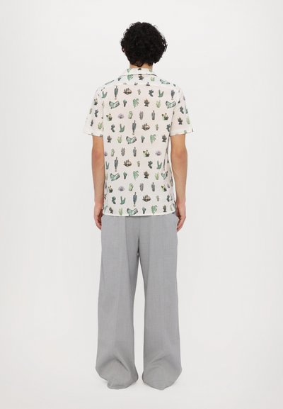 Camisa de manga corta con fondo blanco, adornada con un estampado colorido de cactus, combinada con pantalones de pierna ancha grises.