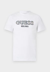 Weißes Baumwoll-T-Shirt mit blauer gestickter Aufschrift "GUESS EST. 1981" auf der Brust. Kurze Ärmel und Rundhalsausschnitt.