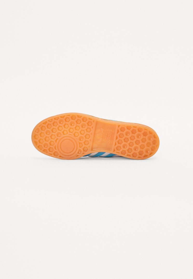 Semelle de basket en caoutchouc présentant un motif hexagonal orange, avec des accents rayés bleu et blanc sur le bord supérieur.