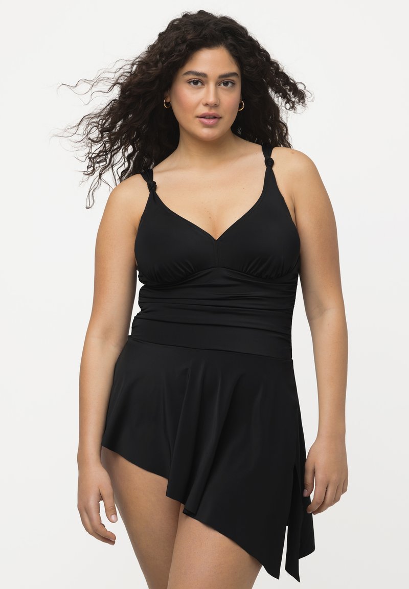 Costume da bagno nero con corpo aderente, scollo a V e spalline regolabili, abbinato a una gonna asimmetrica fluente.