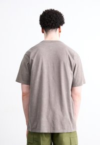 Brun bomulds T-shirt med afslappet pasform og korte ærmer, der viser en let struktureret overflade, parret med olivengrønne cargoshorts.