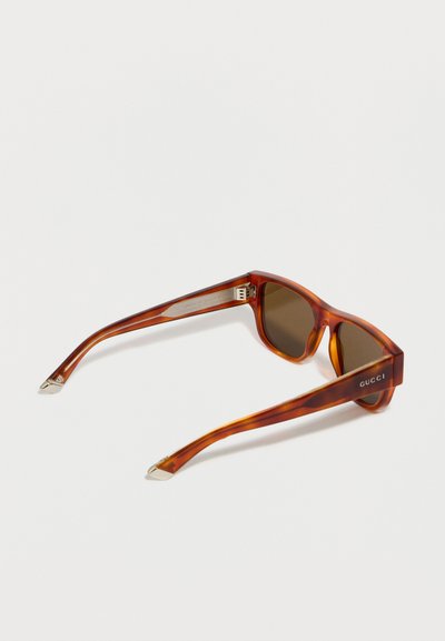 Lunettes de soleil Gucci écaille de tortue avec verres rectangulaires marron et accents argentés sur les embouts des branches et les charnières.