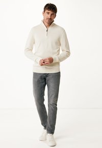 Krämfärgad tröja med halvdragkedja i kragen, ribbade ärmslut och fåll, ihop med grå jeans och vita sneakers. Slät textur och figursydd design.