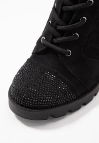 Stivale alla caviglia in suede nero con punta arrotondata, decorato con strass neri nella parte anteriore, dotato di lacci robusti e suola testurizzata.