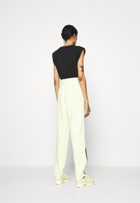 Black sleeveless top, light green joggers with a relaxed fit, and white sneakers with yellow accents. Smooth texture and modern design.