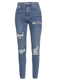 Jeans ajustados de talle alto en denim azul con detalles desgastados, que incluyen grandes desgarros en la parte delantera. Diseño clásico de cinco bolsillos.