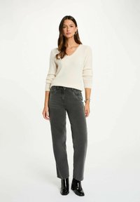 Maglione a V crema in morbido maglione, abbinato a jeans grigi scuri a vita alta e stivaletti neri con tacco. Design semplice e dalla vestibilità rilassata.