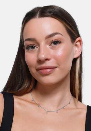 Silberne Halskette mit kleinen sternförmigen Akzenten, die ein filigranes Design aufweist. Wird um den Hals getragen und eignet sich gut zum Layering.