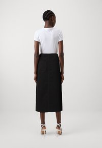 Jupe midi en denim noir avec une coupe droite, couture centrale au dos, et deux poches au dos. Associée à un t-shirt ajusté blanc et des talons à lanières blancs.