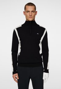 Svart zip-up tröja med vita accentremsor på axlarna och ärmarna. Tillverkad av ett strukturerat material med en figurnära design. Har logotyp.