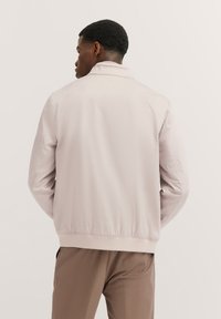 Helle rosa Bomberjacke mit Stehkragen, elastischen Bündchen und Saum. Glattes Material mit minimalen Nähten, von hinten gezeigt.