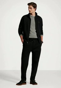 Čierna bunda na zips cez sivý sveter, v kombinácii s čiernymi nohavicami jogger a tmavými teniskami, s voľným strihom a jednoduchým dizajnom.