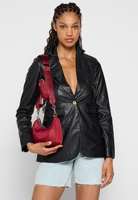 Sort læderjakke med en enkelt guldknap, parret med en lille rød taske med skulderrem, iført med lyse denimshorts.