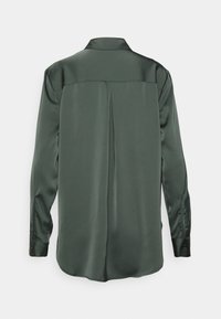 Chemise satinée vert foncé à manches longues vue de dos avec un pli central et des poignets boutonnés sur fond blanc.
