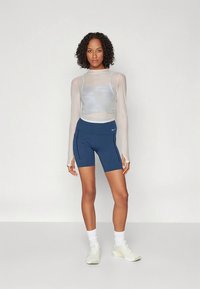 Top leve e transparente de manga comprida por cima de calções azul-marinho de cintura alta com bolsos laterais, combinados com ténis brancos e meias até ao meio da perna.