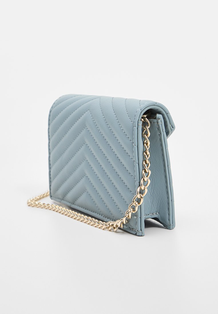 Bolso bandolera de imitación cuero acolchado en azul claro con una cadena dorada y un patrón de zigzag. Presenta una forma estructurada y una base sólida.