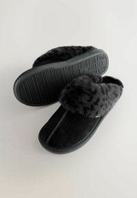 Pantofole nere in suede con una fascia in morbido pelliccia sintetica nera. Suola in gomma spessa con texture scanalata. Dettagli cuciti lungo il centro.