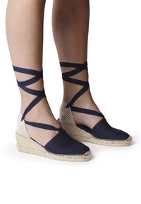 Espadrilles en toile marine avec straps au niveau de la cheville, semelle compensée en fibres naturelles tressées, bout arrondi et détail en texture sur le dessus.