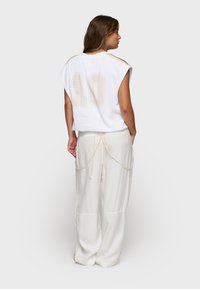 Top blanco sin mangas con el número "10" en beige en la parte posterior, combinado con pantalones holgados en color crema con detalles de cordón.