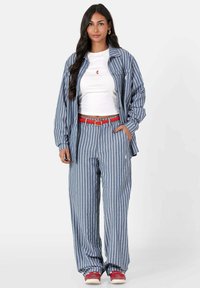 Blauw-wit gestreepte oversized blouse gecombineerd met bijpassende broek, verfraaid met een rode riem. De outfit heeft een ontspannen pasvorm en een grote silhouet.